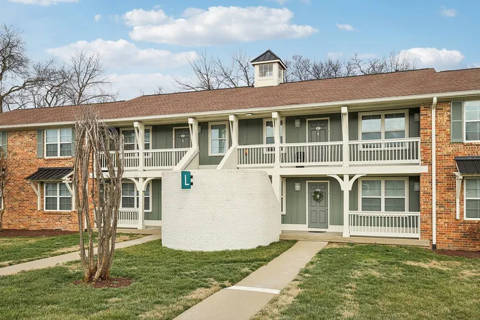 Charming two-story apartment complex with elegant balconies, a welcoming entrance, and beautifully landscaped surroundings under a bright blue sky.