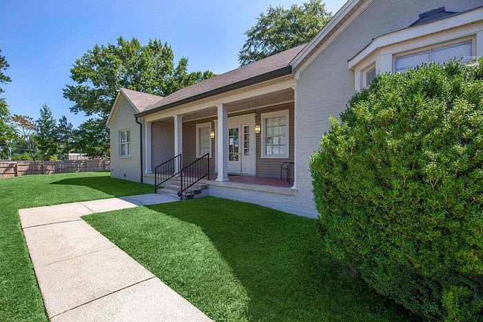 Charming single-story home with a welcoming porch, surrounded by lush greenery and a manicured lawn.