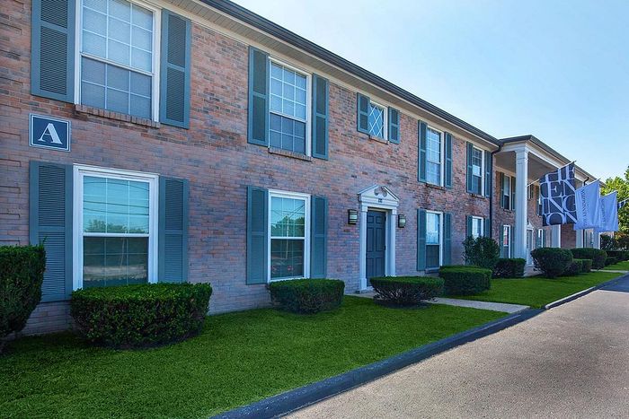 Charming brick apartment building with colonial-style architecture, featuring well-maintained landscaping and large windows, perfect for a cozy living environment.
