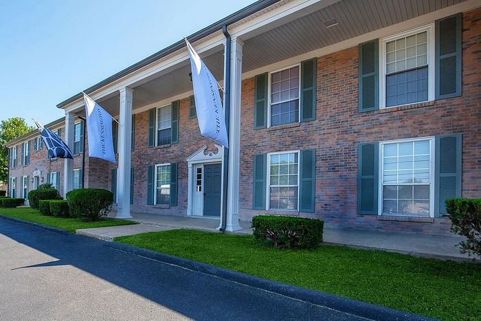 Charming brick apartment building with elegant pillars and vibrant green landscaping under a clear blue sky.
