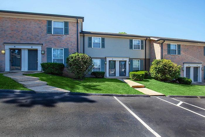 Charming two-story apartment building with classic brick facade, lush green landscaping, and convenient front entrances, perfect for comfortable living.
