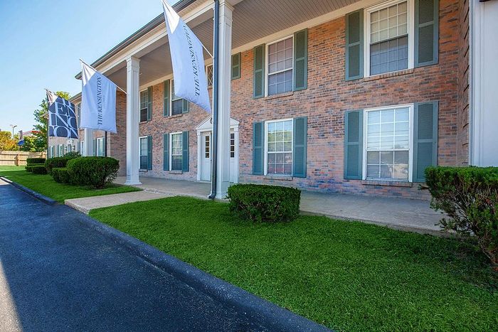 Charming brick apartment building with elegant columns and well-maintained landscaping, featuring the Kensington flag for a welcoming entrance.