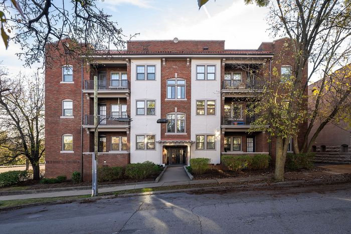 Charming brick apartment building with classic architecture and inviting balconies, surrounded by lush trees on a tranquil street.