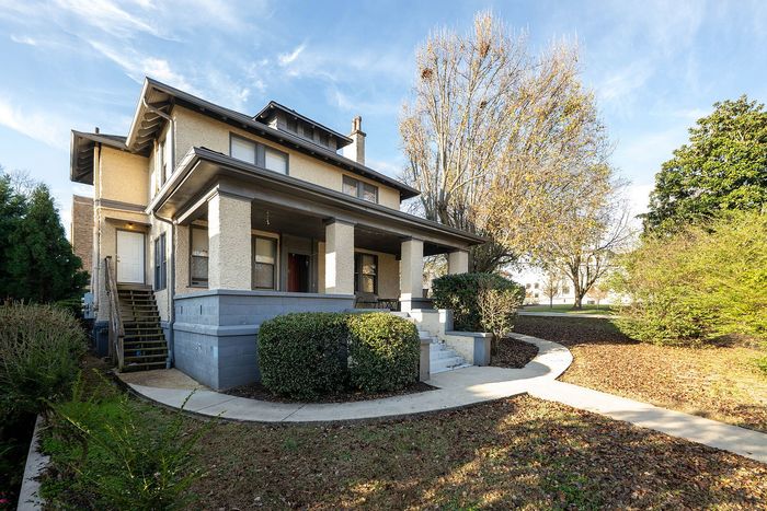 Charming two-story house with a spacious front porch, nestled amidst lush greenery and a well-maintained garden path.