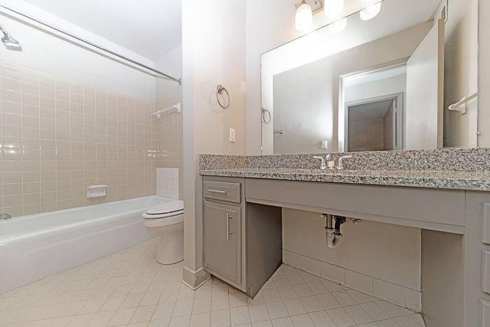 Modern bathroom with elegant granite countertop, spacious vanity, and a sleek bathtub with tiled walls.
