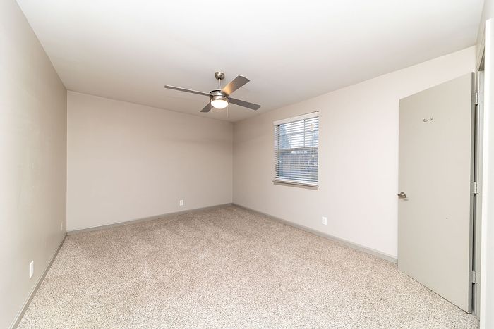 Bright, airy bedroom with plush carpet, modern ceiling fan, and large window for natural light.