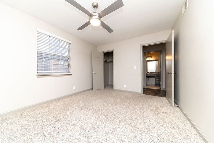 Bright, inviting bedroom featuring plush carpeting, modern ceiling fan, and ample natural light with access to an elegant ensuite bathroom.