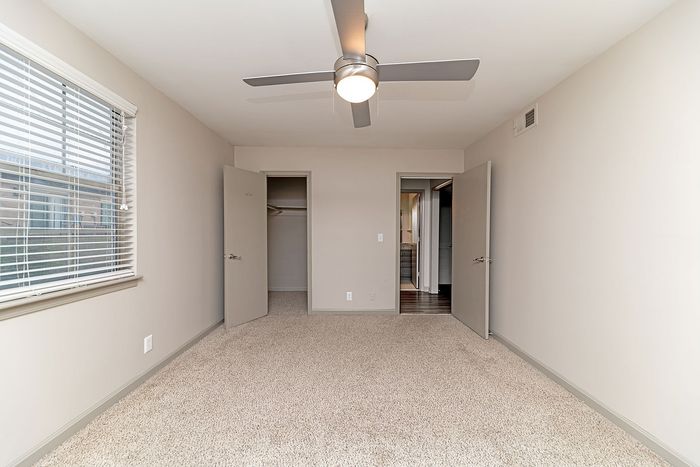 Inviting bedroom with plush carpet, modern ceiling fan, and ample natural light from large window.