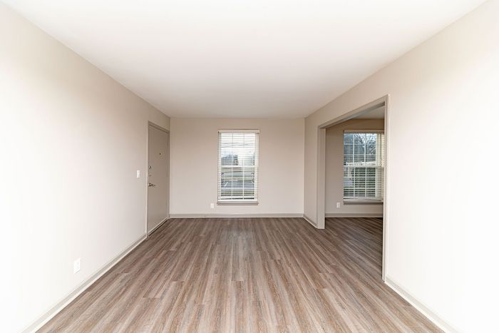 Bright, open living space featuring elegant hardwood flooring and modern window blinds, perfect for a cozy, versatile setup.