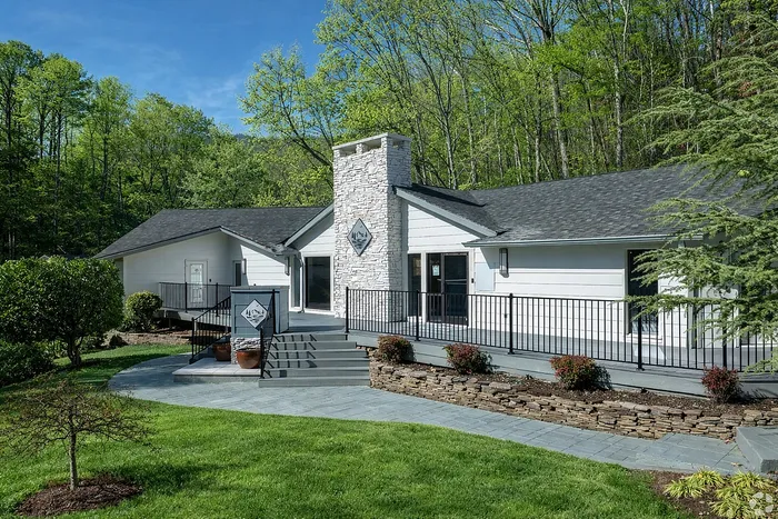 Charming modern home surrounded by lush greenery, featuring elegant white stone exterior and inviting front steps.