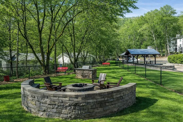 Charming outdoor seating area with a fire pit, surrounded by lush greenery and cozy benches, perfect for relaxation.