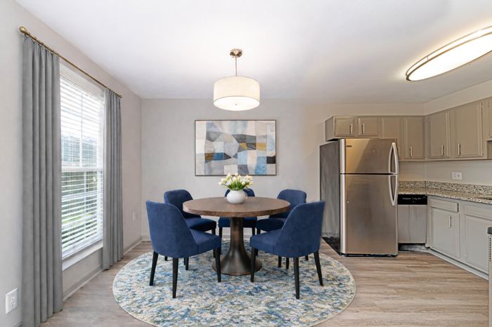 Modern dining area with round wooden table, stylish blue chairs, and contemporary kitchen featuring stainless steel appliances.