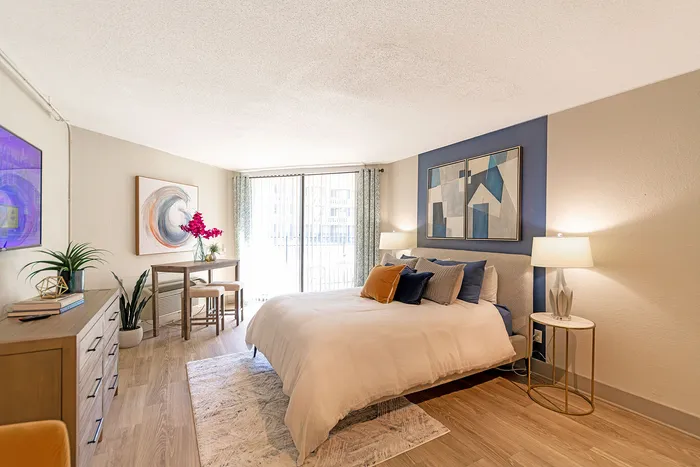 Bright and stylish bedroom with modern decor, featuring a cozy bed, chic artwork, and a sunlit balcony view.