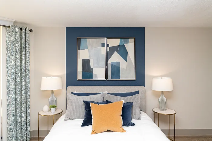 Cozy bedroom with stylish geometric artwork, plush pillows, and elegant bedside lamps, creating a serene retreat.