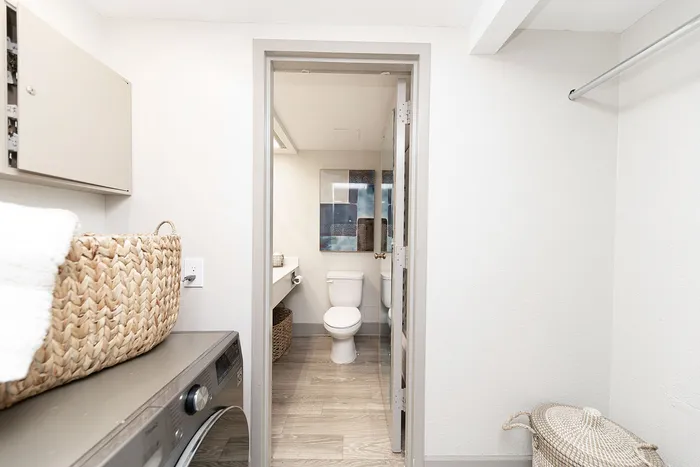 Bright and modern laundry room with a washer, woven baskets, and a sleek adjoining bathroom.