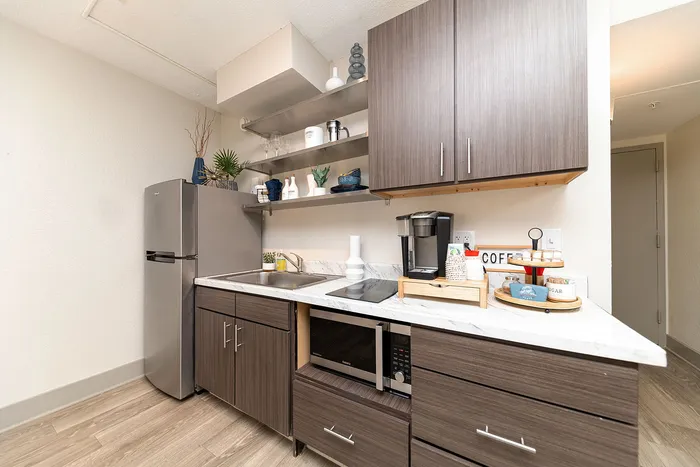 Contemporary kitchenette with sleek dark wood cabinets, modern appliances, and stylish open shelving for a chic and functional living space.