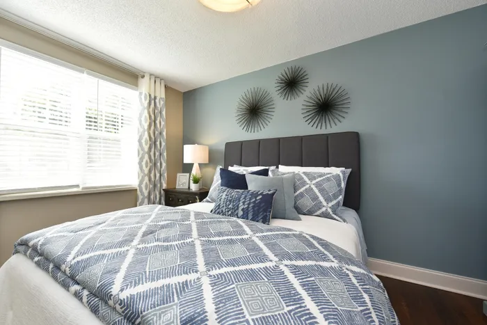 Bright and inviting bedroom with elegant decor, featuring a plush bed with blue patterned bedding, modern wall art, and abundant natural light through large windows.