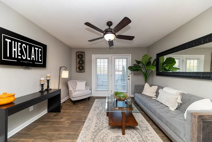 Chic living room featuring a plush gray sofa, stylish decor, modern ceiling fan, and natural light from double doors at The Slate at Ninety-Six.