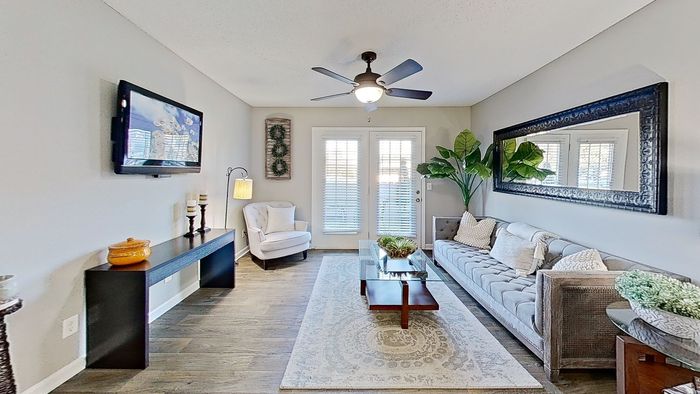 Chic living room featuring a cozy gray sofa, elegant wall mirror, and inviting natural light from glass doors, complemented by stylish decor and a ceiling fan.