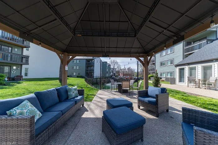 Inviting outdoor patio with comfortable wicker furniture under a stylish gazebo, overlooking lush green lawns and modern apartment buildings.