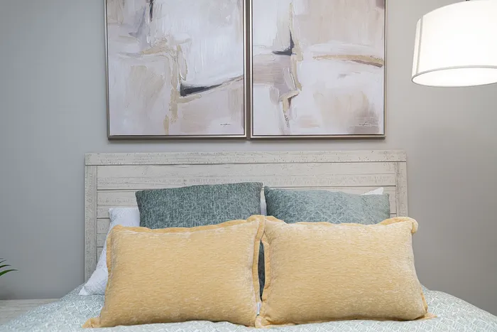 Chic bedroom setup with elegant abstract paintings, plush pillows in soothing hues, and a stylishly textured wooden headboard.