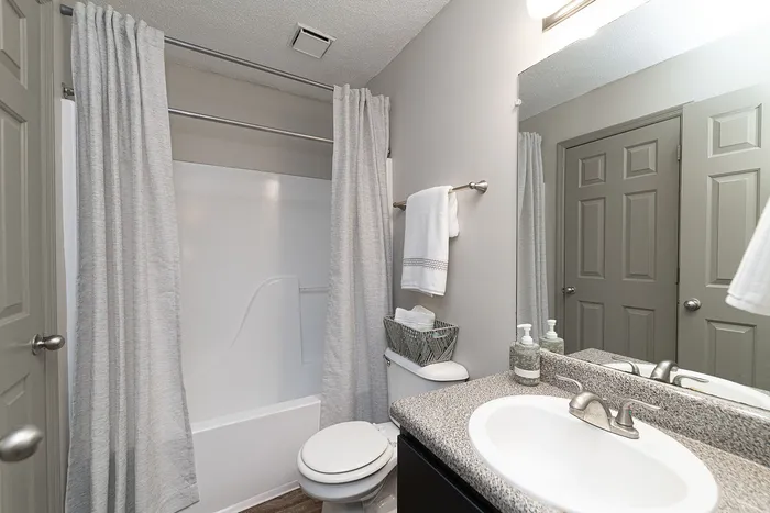 Modern bathroom featuring a sleek sink with a granite countertop, elegant fixtures, and a pristine bathtub with soft gray shower curtains.