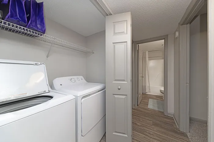 Modern laundry area with sleek washer and dryer adjacent to a bright bathroom, featuring neutral tones and elegant wood flooring.
