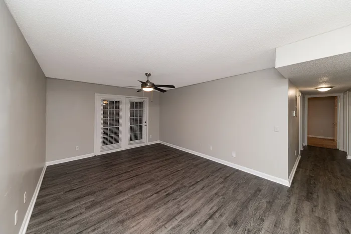 Spacious living room featuring sleek hardwood floors, modern ceiling fan, and elegant French doors leading to a cozy hallway.