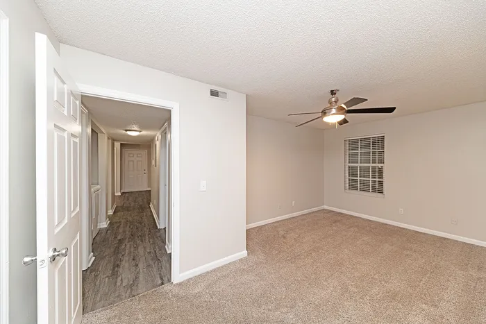 Inviting room with plush carpet, a ceiling fan, and a view down a hallway with elegant wood flooring.