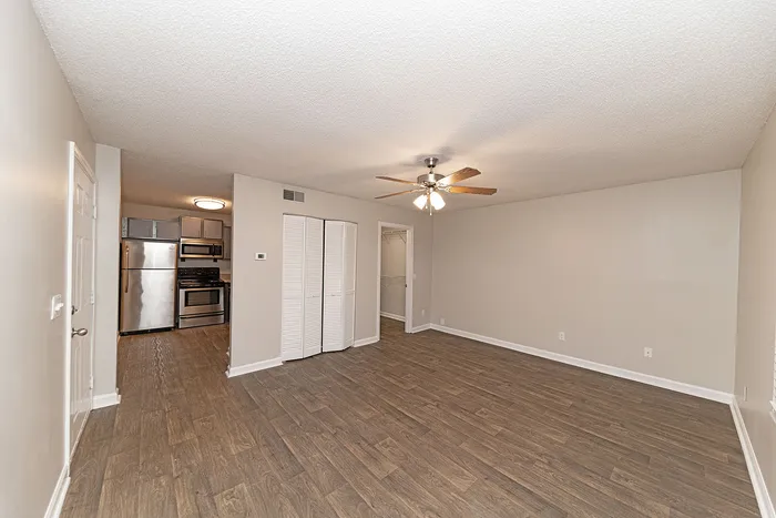 Spacious open-plan living area with modern ceiling fan, hardwood flooring, and sleek stainless steel kitchen appliances.