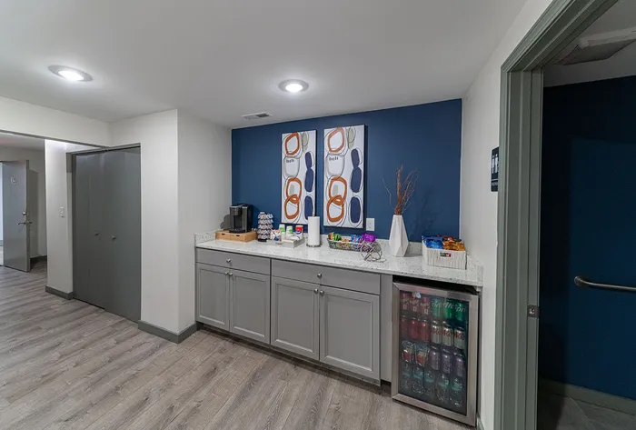 Chic apartment refreshment nook with sleek cabinetry, beverage fridge, and modern art decor, offering a stylish welcome.