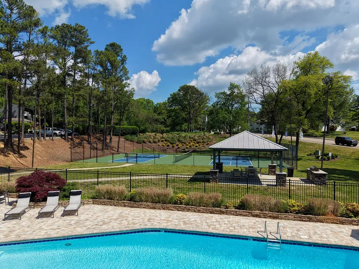Inviting outdoor view featuring a sparkling swimming pool, tennis court, and charming gazebo surrounded by lush greenery under a clear blue sky.