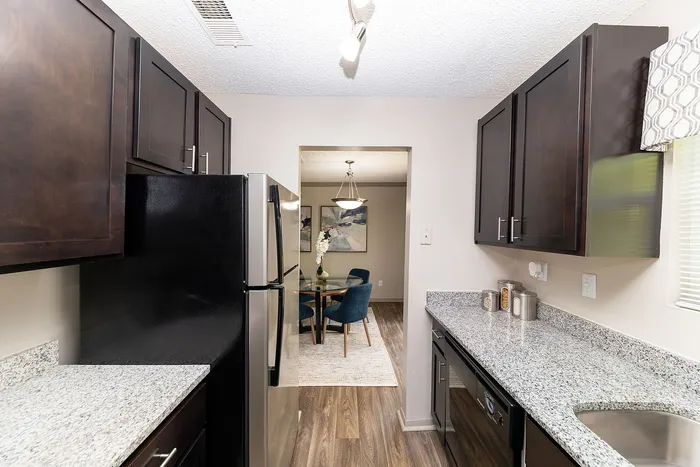 Sleek modern kitchen with elegant dark wood cabinets, stainless steel appliances, and a view into a stylish dining area with plush blue chairs.