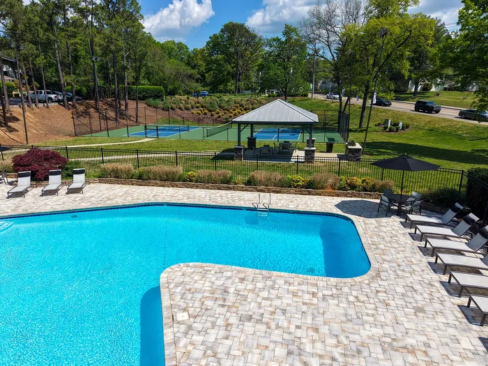 Elegant outdoor area featuring a sparkling swimming pool and adjacent tennis court, surrounded by lush greenery and stylish lounge chairs.