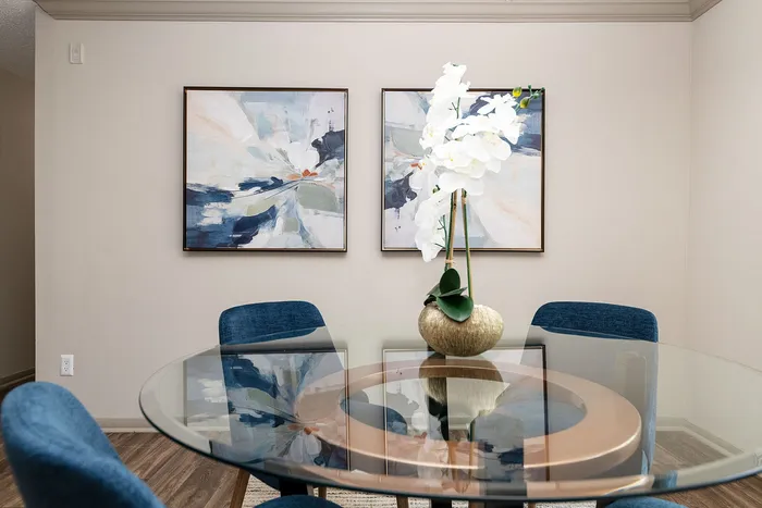 Elegant dining area featuring a modern glass table with plush blue chairs and contemporary abstract art on the walls, complemented by a chic orchid centerpiece.