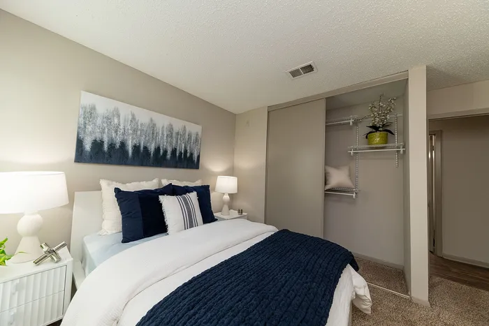 Cozy bedroom featuring a plush bed with navy blue accents, stylish abstract artwork, and an organized open closet.