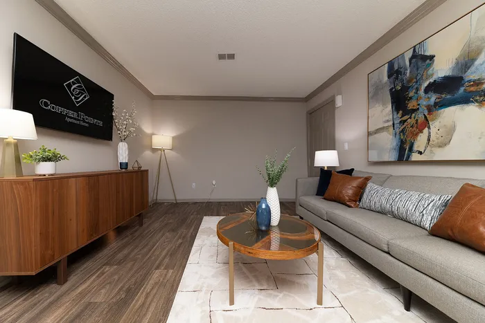 Contemporary living room with elegant decor, featuring a plush gray sofa, wooden coffee table, chic artwork, and modern lighting at Copper Pointe Apartment Homes.