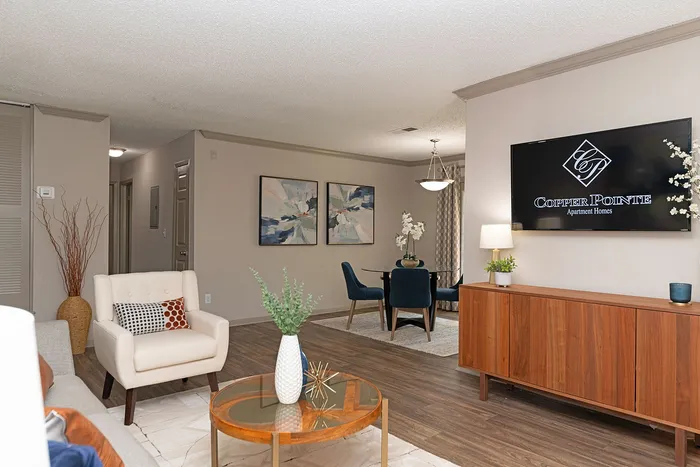 Chic living room with elegant decor at Copper Pointe Apartment Homes, featuring a cozy armchair, modern glass dining table, and sleek wooden floor, perfect for stylish living.