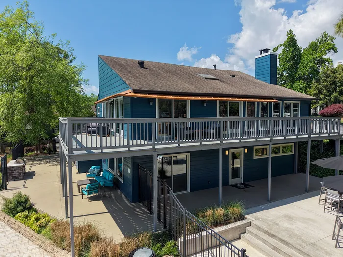 Charming two-story home with a spacious wrap-around balcony, modern exterior design, and lush greenery in a serene setting.