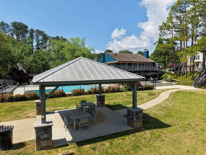 Inviting outdoor area with a cozy gazebo next to a sparkling pool, surrounded by lush greenery and modern seating, perfect for relaxation.