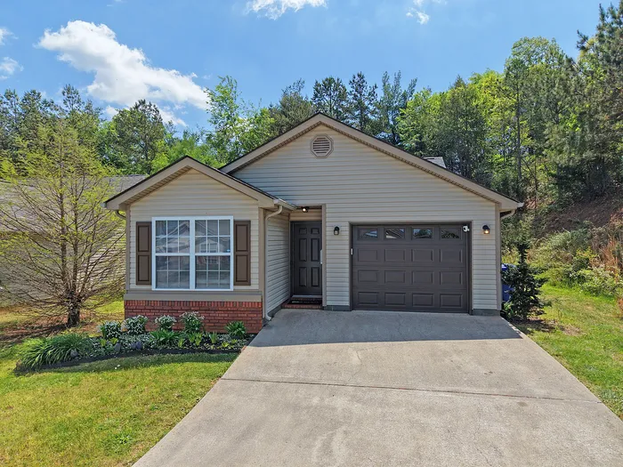 Charming single-story home with attached garage, nestled in a lush, green setting with a welcoming front yard.