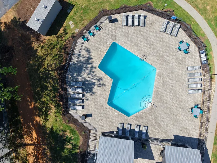 Inviting aerial view of a uniquely shaped swimming pool surrounded by stylish sun loungers and bright green lawns, perfect for relaxation and leisure.