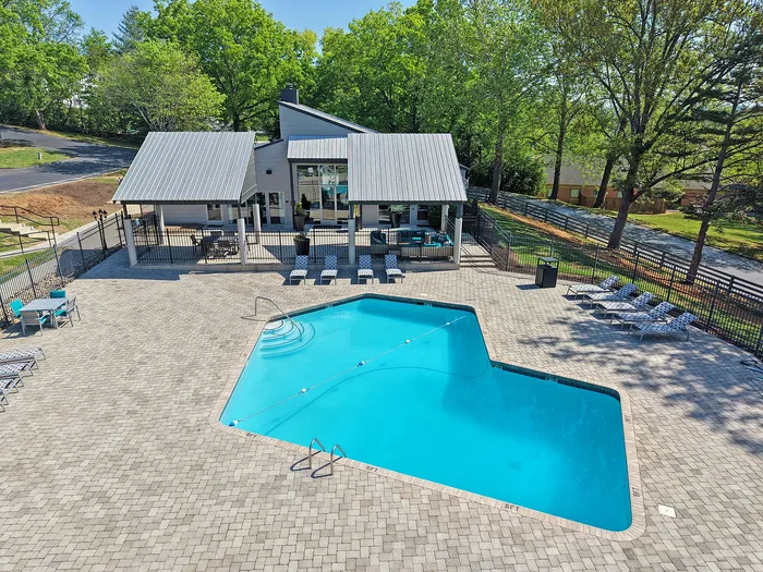 Inviting outdoor pool area with stylish lounge chairs, surrounded by lush greenery and a modern clubhouse under a clear blue sky.
