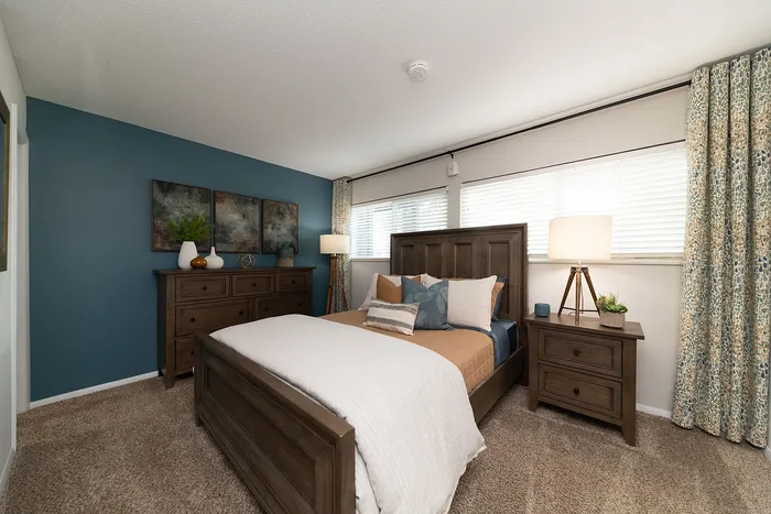 Cozy bedroom with elegant decor, featuring a wooden bed and dresser, soft carpeting, and modern art on a teal accent wall.