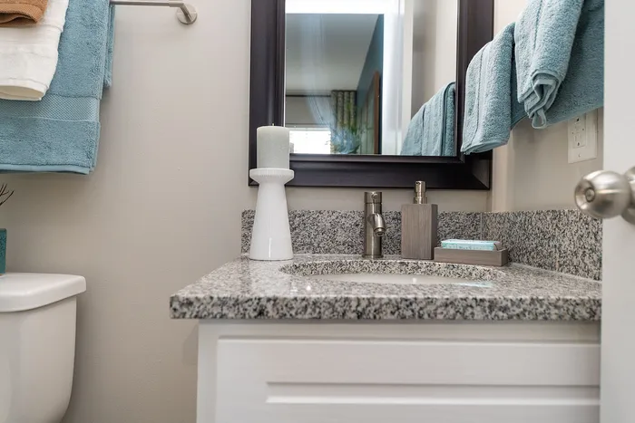 Elegant bathroom with granite countertop, stylish fixtures, and neatly arranged teal towels, exuding modern luxury.
