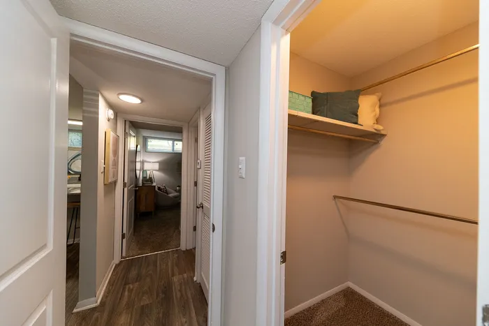 Inviting apartment hallway leading to a cozy bedroom, featuring a spacious walk-in closet with ample shelving.