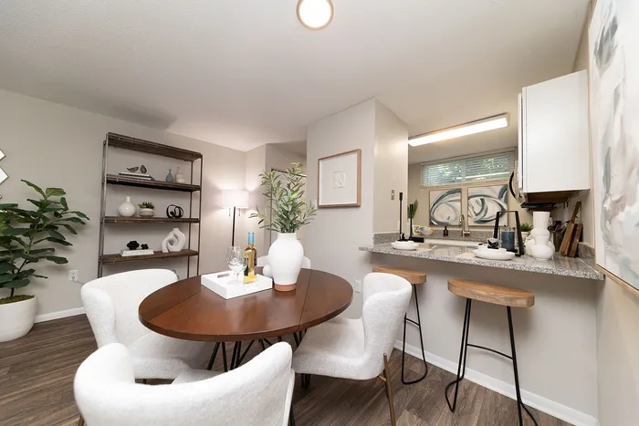 Inviting dining area with elegant round wooden table, plush white chairs, and a modern kitchen countertop with stylish bar stools, perfect for social gatherings.