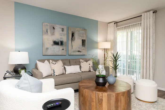 Chic living room with modern decor, featuring a cozy gray sofa, stylish armchair, abstract art on a blue accent wall, and large windows draped with elegant curtains inviting natural light.