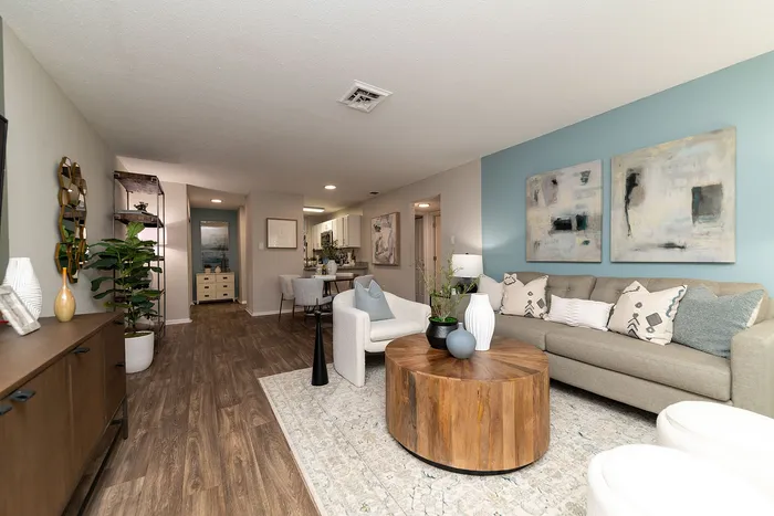 Elegant living room with modern decor, featuring a cozy beige sofa, stylish wooden coffee table, and tasteful abstract art on soft blue walls.