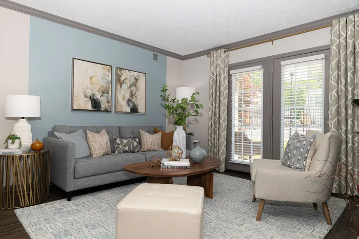 Modern living room with elegant decor, featuring a cozy gray sofa, stylish armchair, and chic coffee table under soft lighting by large windows.